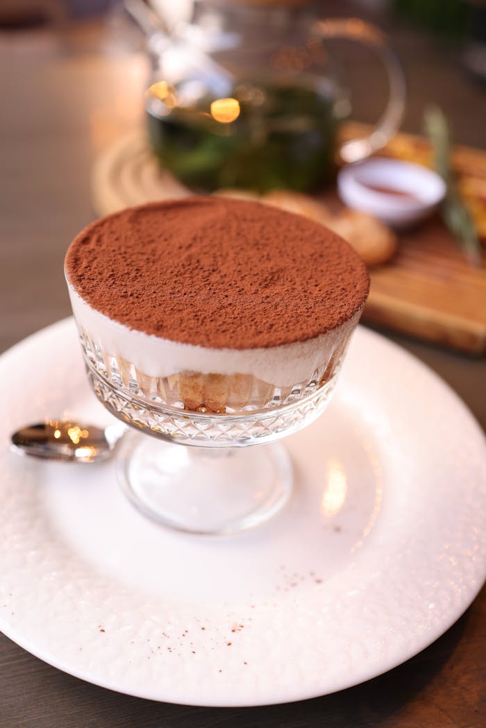 A delicious tiramisu in a glass cup, elegantly served with a spoon on a white plate.